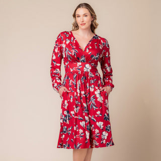 The plus size model is wearing the Flirty Flounce Wrap Dress by Kiyonna.  The navy blue wrap dress has pink and copper flowers throughout.